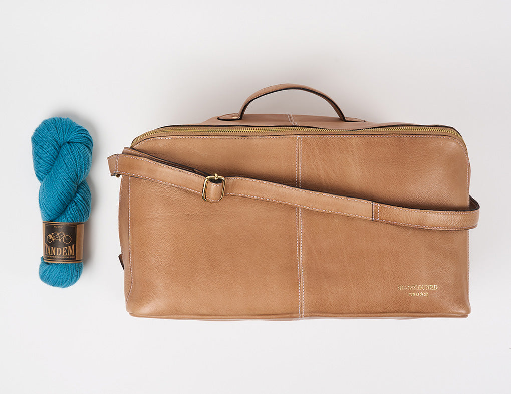 This image shows Project 40 - Taupe from Re:Designed. The project bag stands on a white background. A skein of blue Tandem from West Wool is placed next to the bag. 