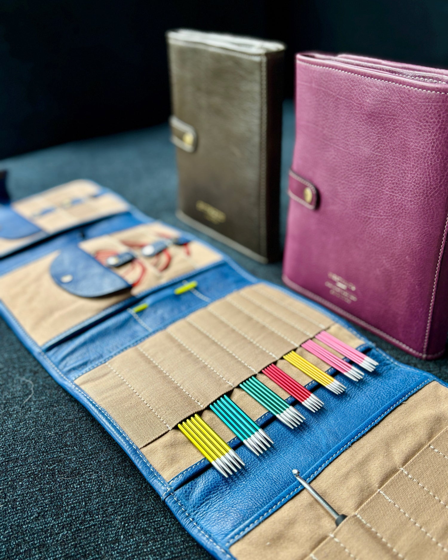 This image shows 3 project 14 in aubergine, denim, and dark green from Re:Designed, laid on a sofa and filled with needles. 