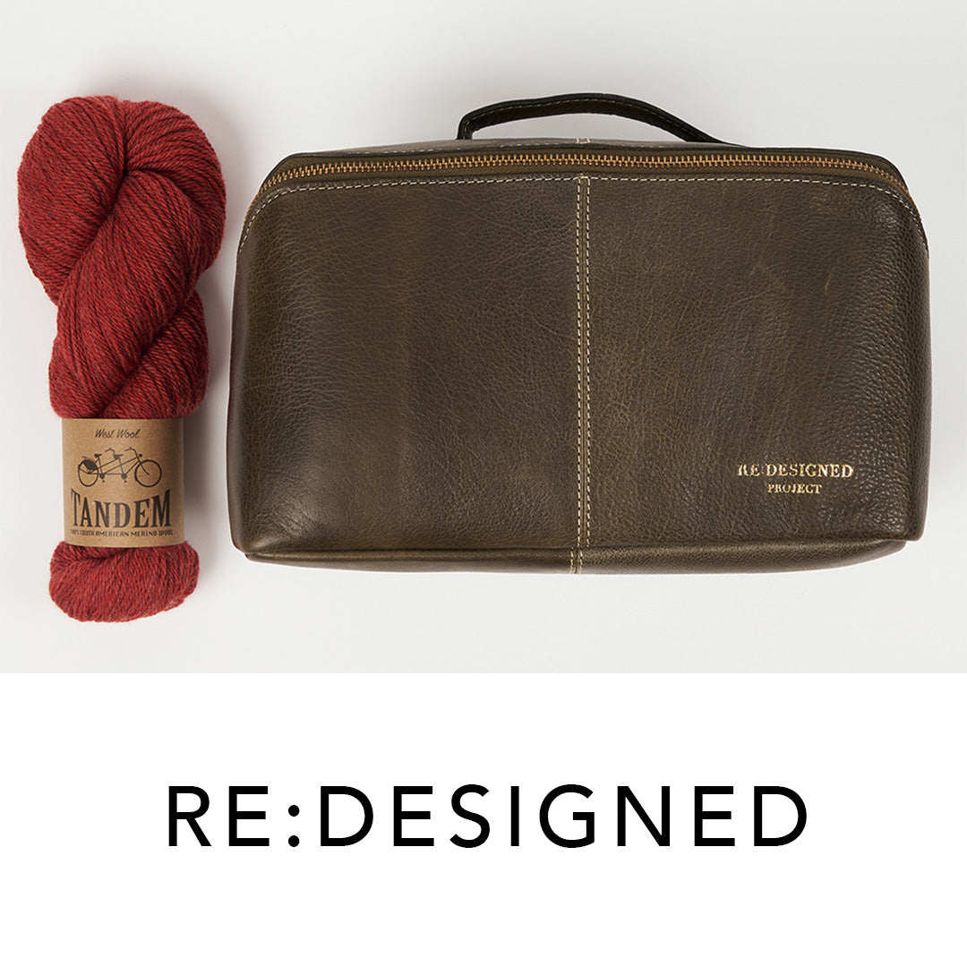 This image shows a dark green project bag from Re:Designed next to a skein of West Wool Tandem in red. Underneath, the text says: Re:Designed. 