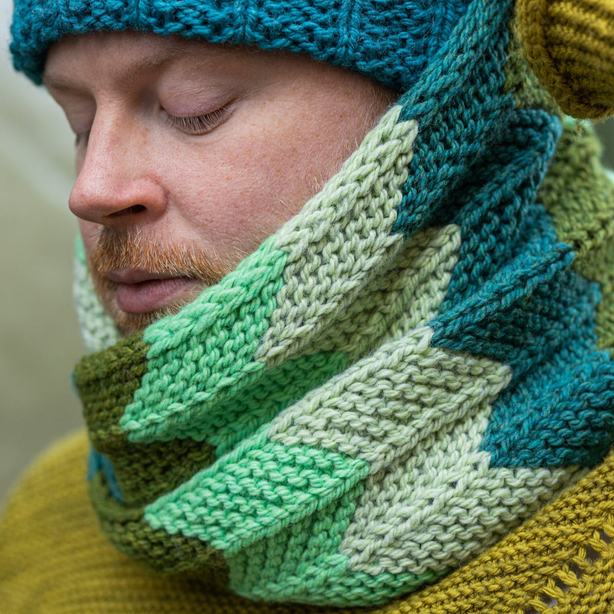 This image shows Stephen West wearing a beautifully knitted cowl in green gradients. The cowl is a Retro Chevron Cowl.