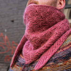 Stephen West wearing a hand knitted sample of a small shawl in red-pink tones. 