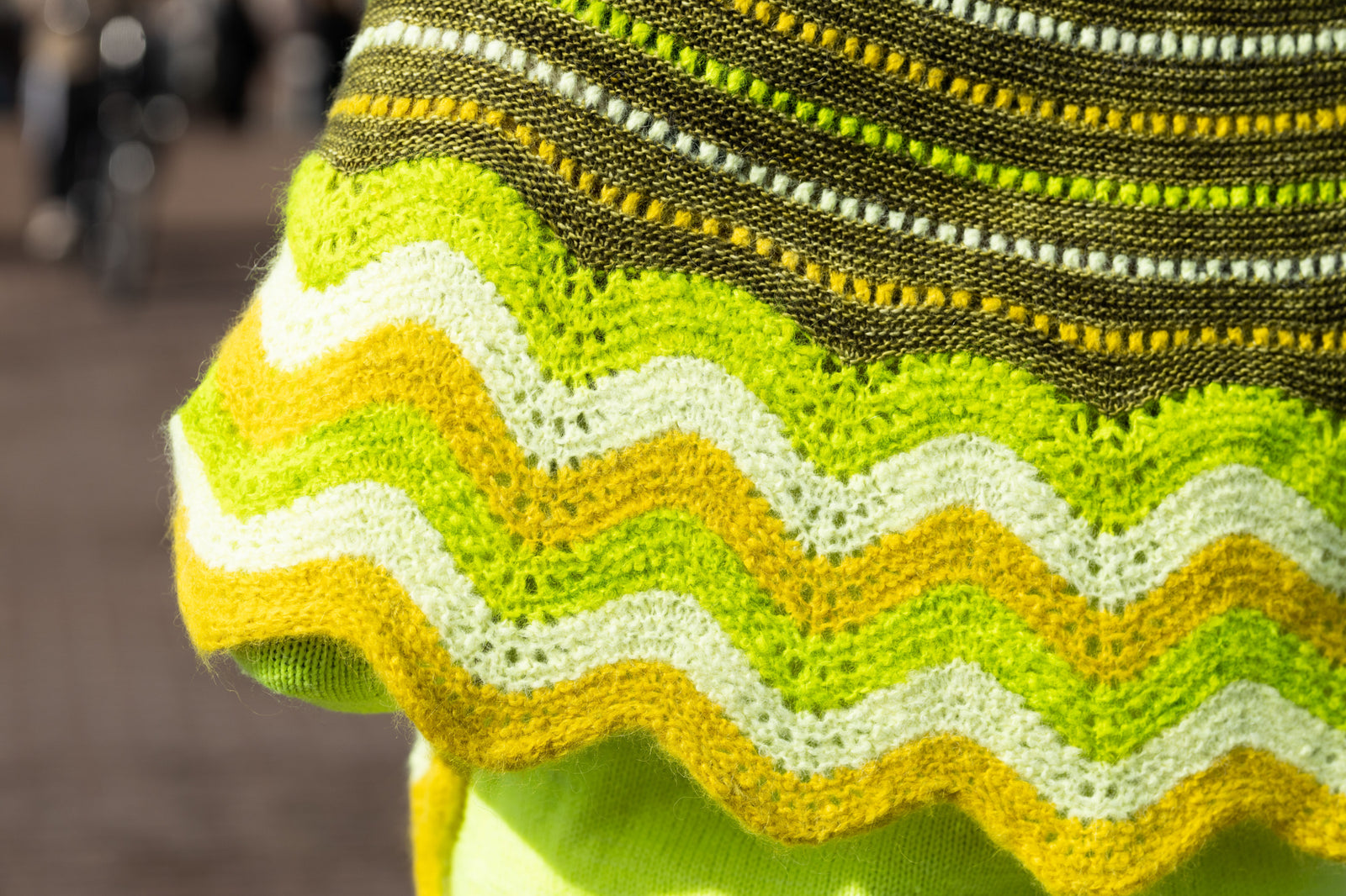 This image shows a  beautifully knitted sample of the Suri Shimmy Shawl in green and yellow gradients. 