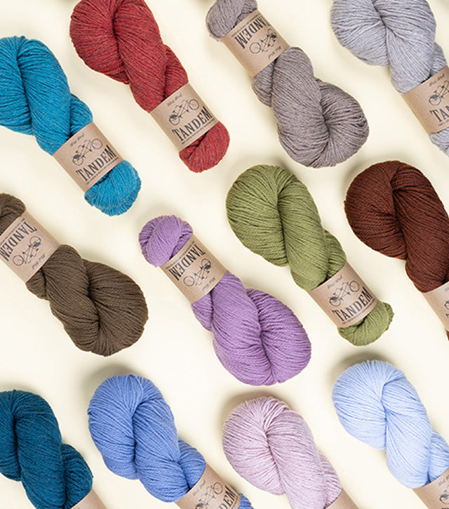 This image shows the variety of new colours of Tandem from West Wool on a pastel yellow background. The colours include brown, coral, orange, blue and green. 