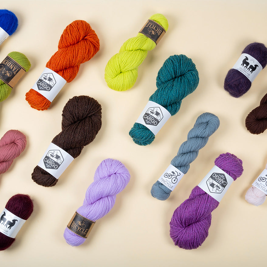 This image shows various skeins of the brand West Wool on a pastel yellow background. The skeins are in various colours and bases (Tricycle, Tandem, Bicycle, Glowhair, Cargo). 