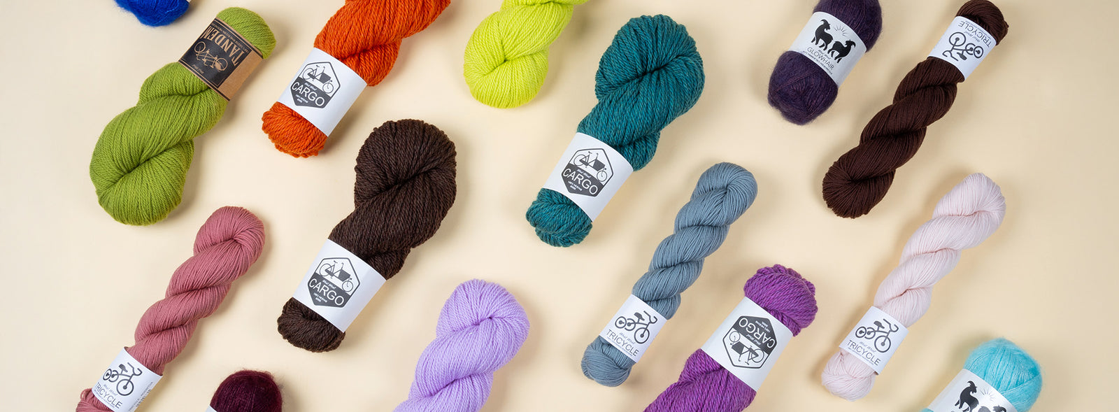 This image shows various skeins of the brand West Wool on a pastel yellow background. The skeins are in various colours and bases (Tricycle, Tandem, Bicycle, Glowhair, Cargo). 