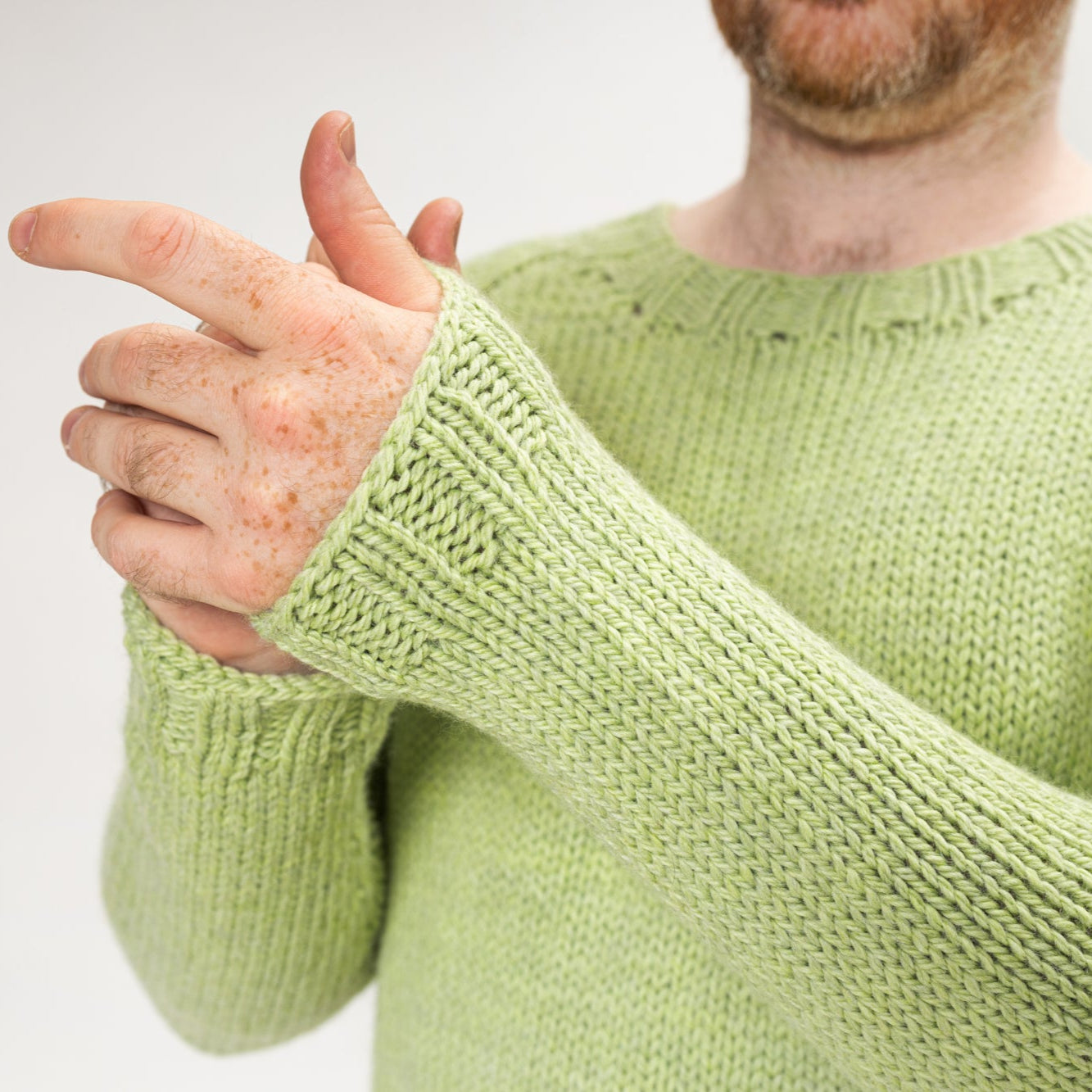 This image shows a detail of Stephen West wearing a beautifully knitted sample of the Chunky Raglan Sweater from Westknits. It was knitted with West Wool Cargo. He stands on a white background. 