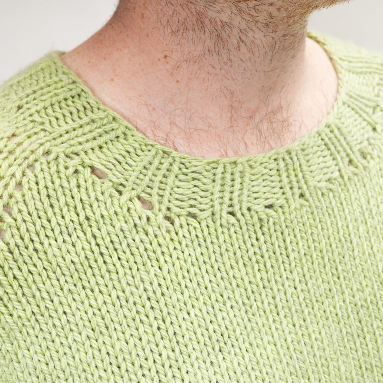 This image shows a detail of Stephen West wearing a beautifully knitted sample of the Chunky Raglan Sweater from Westknits. It was knitted with West Wool Cargo. He stands on a white background. 