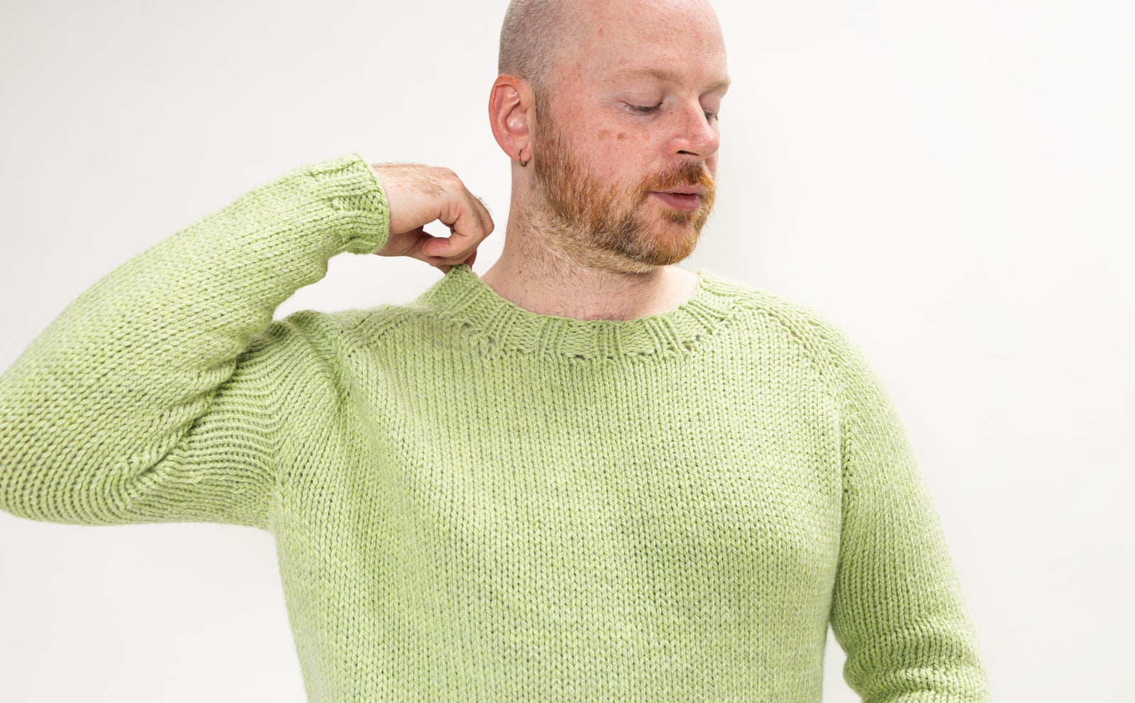 This image shows Stephen West wearing a beautifully knitted sample of the Chunky Raglan Sweater from Westknits. It was knitted with West Wool Cargo. He stands on a white background. 