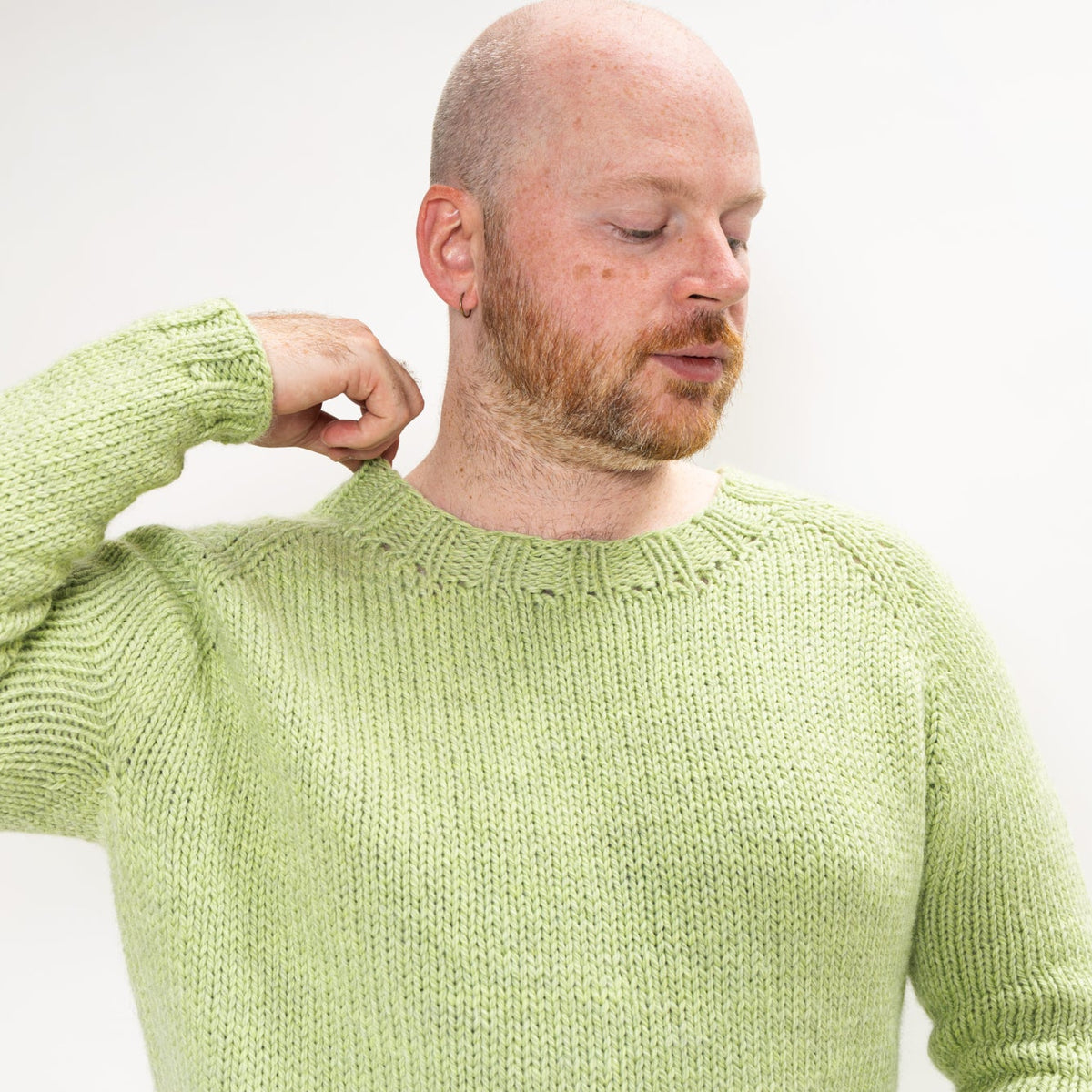 This image shows Stephen West wearing a beautifully knitted sample of the Chunky Raglan Sweater from Westknits. It was knitted with West Wool Cargo. He stands on a white background. 