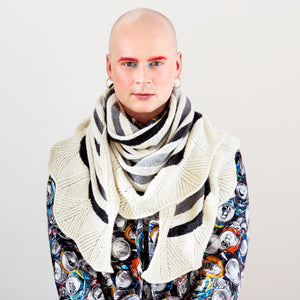 This image shows Stephen West wearing a beautifully knitted sample of the Canal Ring Shawl from Westknits in contrasting grey and white tones. 