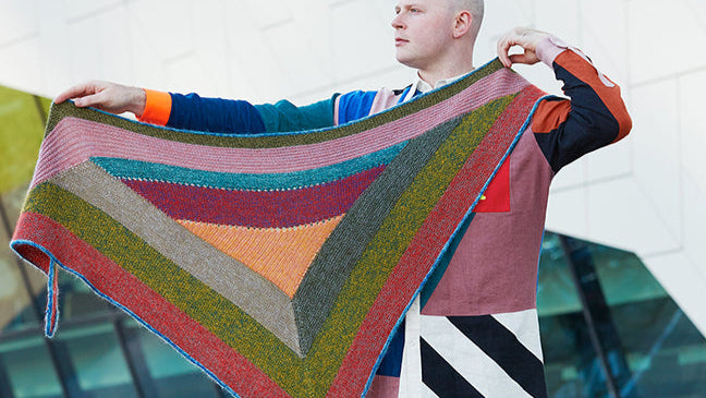 This image shows Stephen West wearing a beautifully knitted sample of the Mohair Mixer Shawl by Westknits in various colours. 