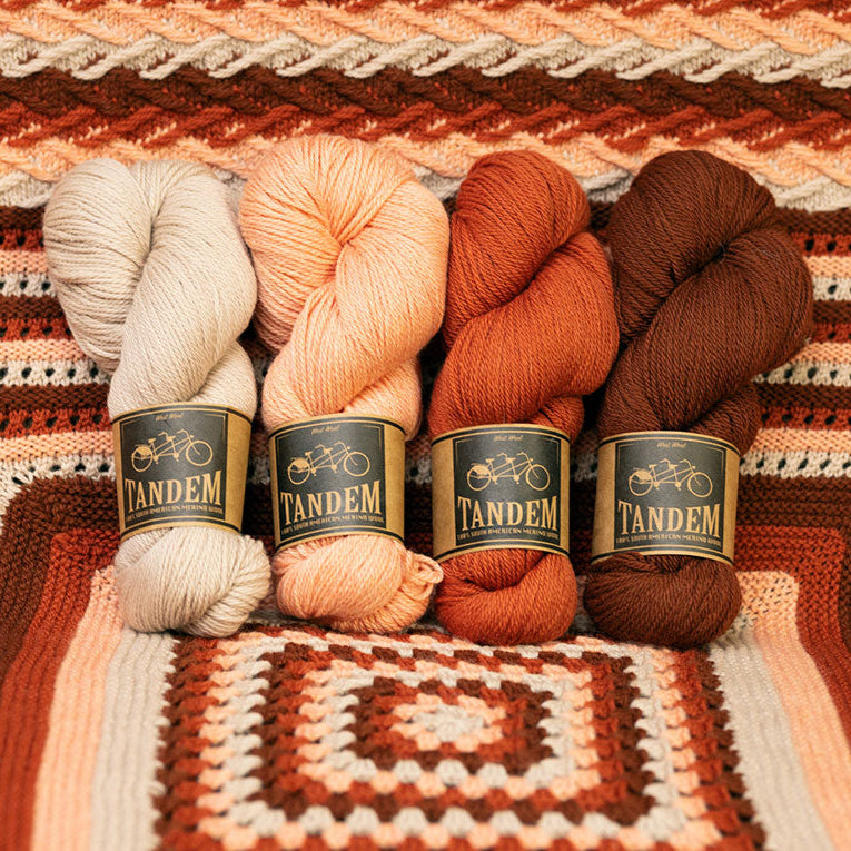 This image shows a beautifully knitted sample of the Geogradient Blanket by Westknits in warm pink and red tones. The yarn used for the sample is laid on top. 