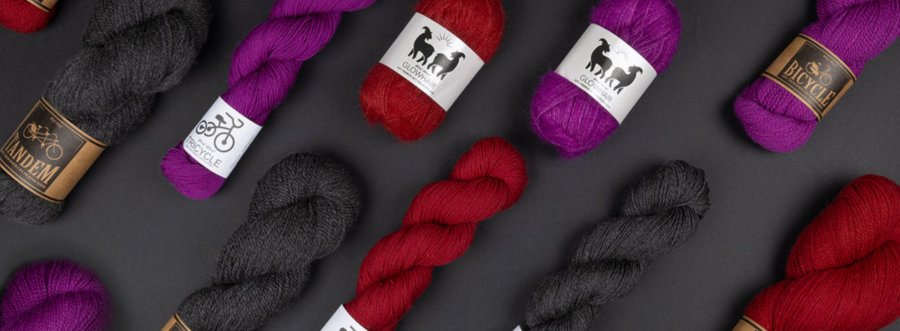 This image shows some West Wool skeins in purple, red, and fuchsia on a black background. It advertises the section of Goth style. 