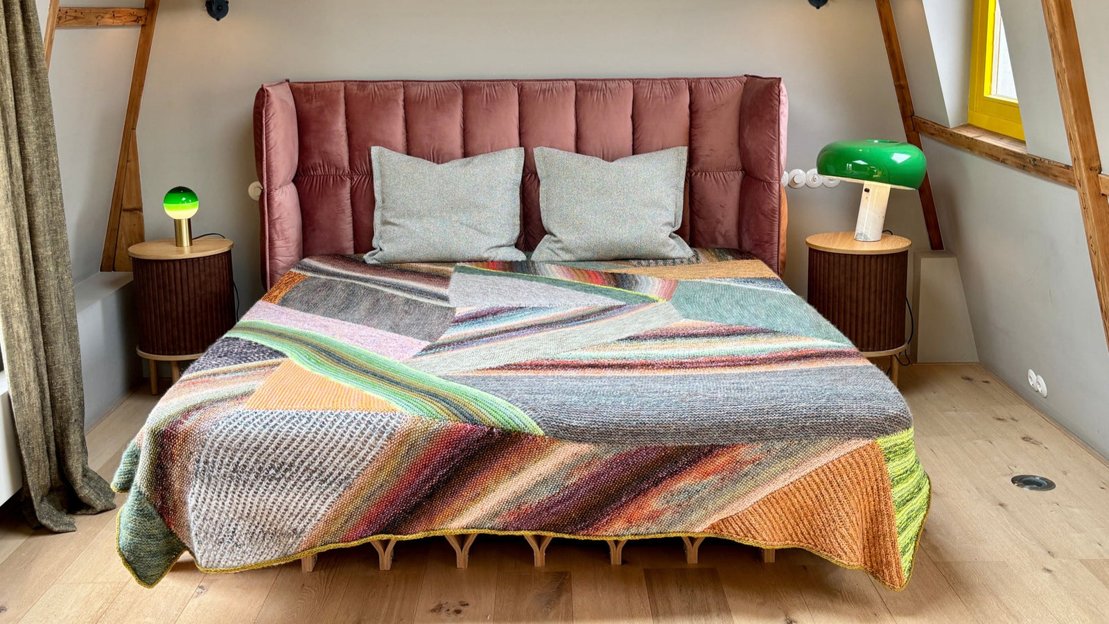 This image shows a beautifully knitted sample of the Marled Magic Blanket by Westknits. The blanket is laid on a bed and it is knitted with a patchwork layout in various colours. 