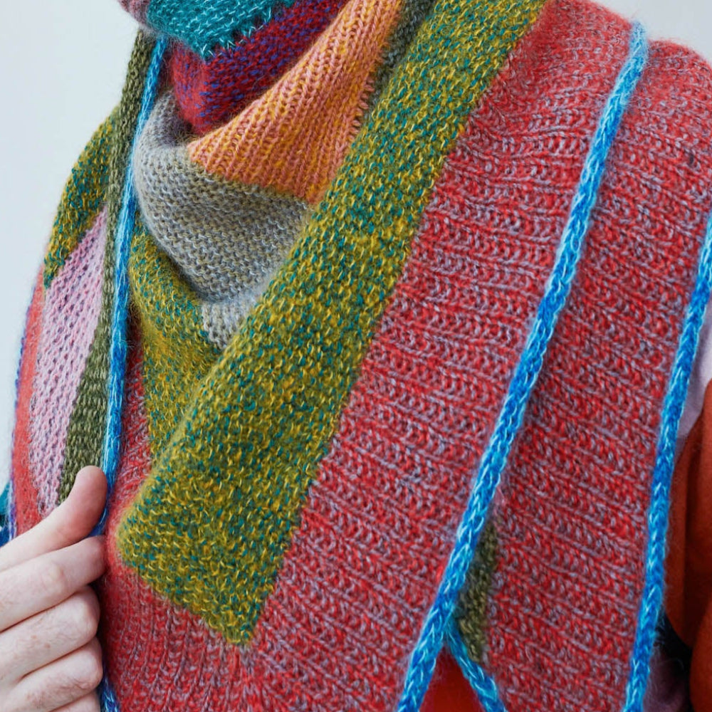 This image shows Stephen West wearing a beautifully knitted sample of the Mohair Mixer Shawl by Westknits in various colours. 