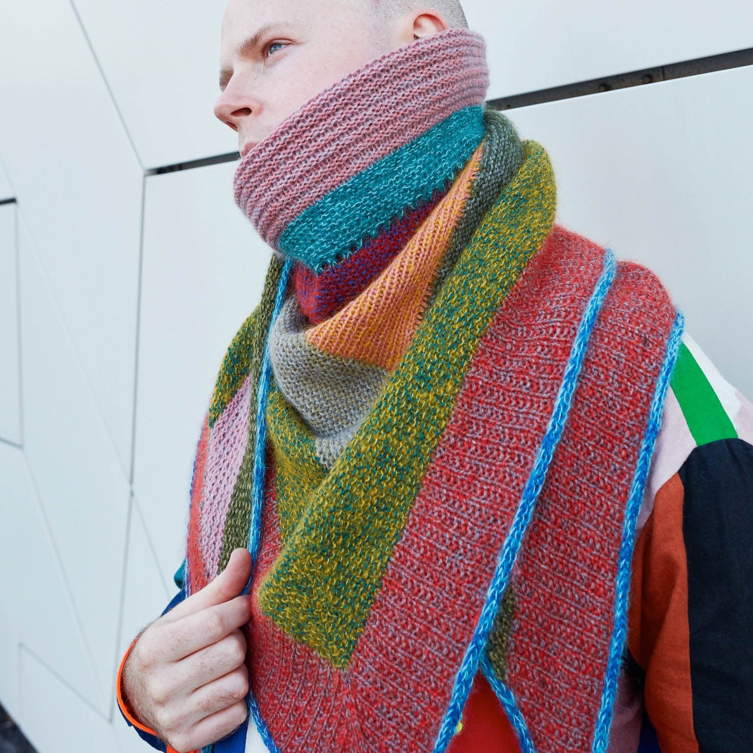 This image shows Stephen West wearing a beautifully knitted sample of the Mohair Mixer Shawl by Westknits in various colours. 