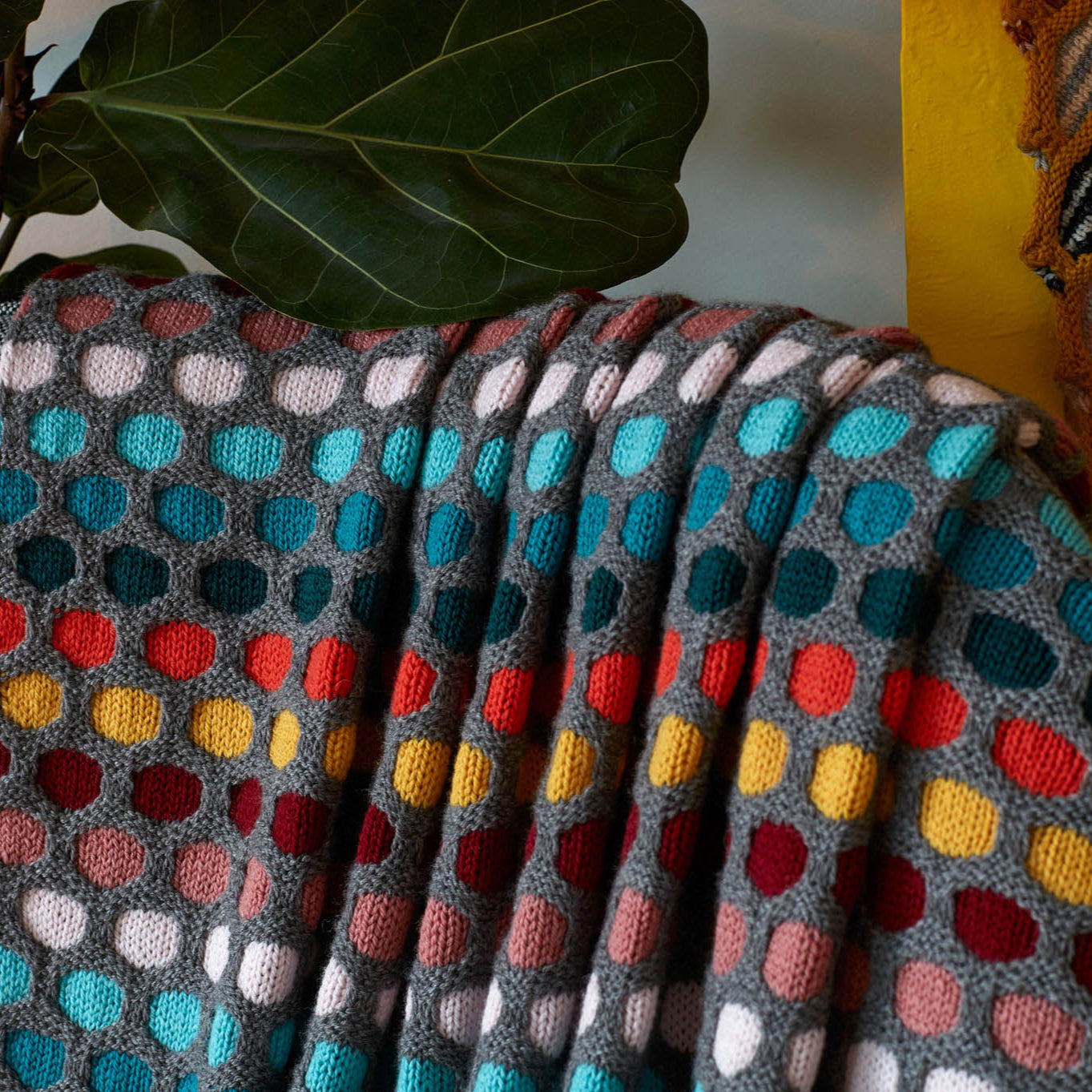 This image shows a detail of a knitted sample of the Painting Honeycombs Blanket by Westknits in various colours, including grey, yellow, orange, blue. 